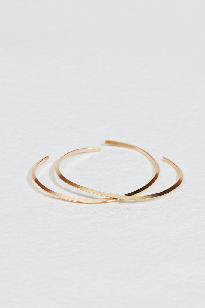 close up of two gold cuff bracelets with knife edge detail