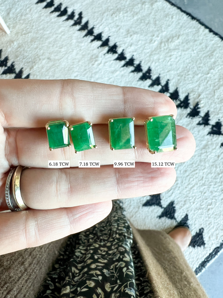 close up of hand holding emerald cut emerald studs in various tcw sizes