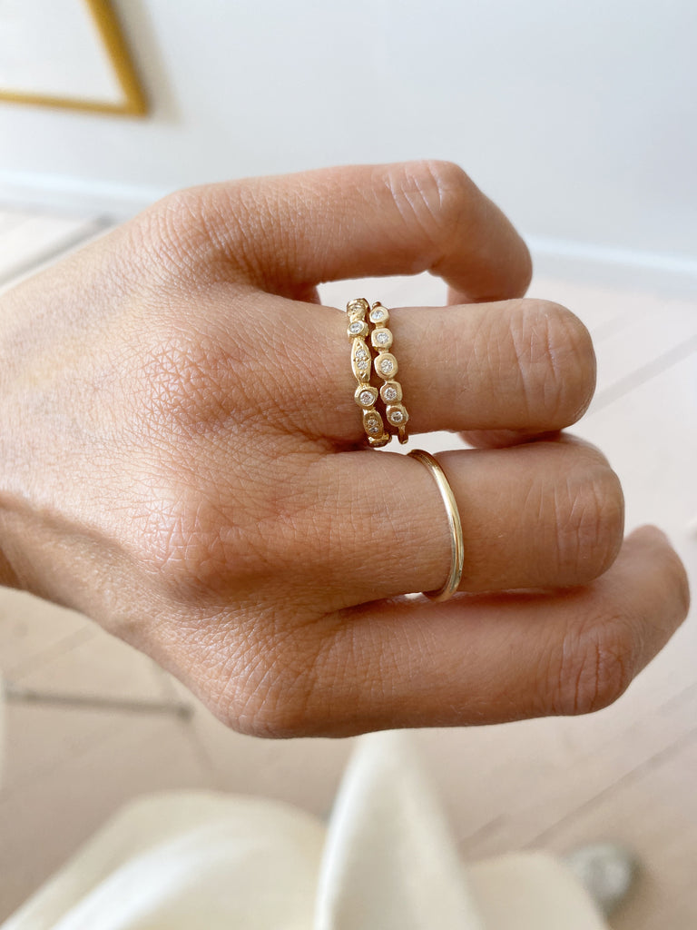 close up of hand wearing gold oval and circle bezel set eternity band with round white diamonds alongside other gold rings