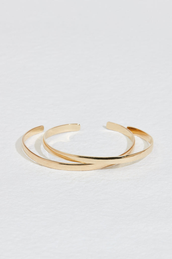 close up of two gold cuff bracelets with rounded edges