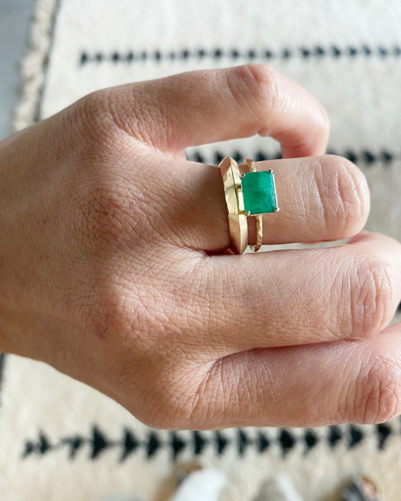 close up of hand wearing knife edge cut gold band alongside other gold ring