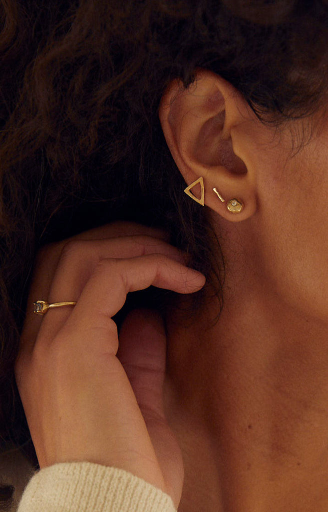 close up of woman wearing gold bezel set round white diamond stud alongside other gold jewelry