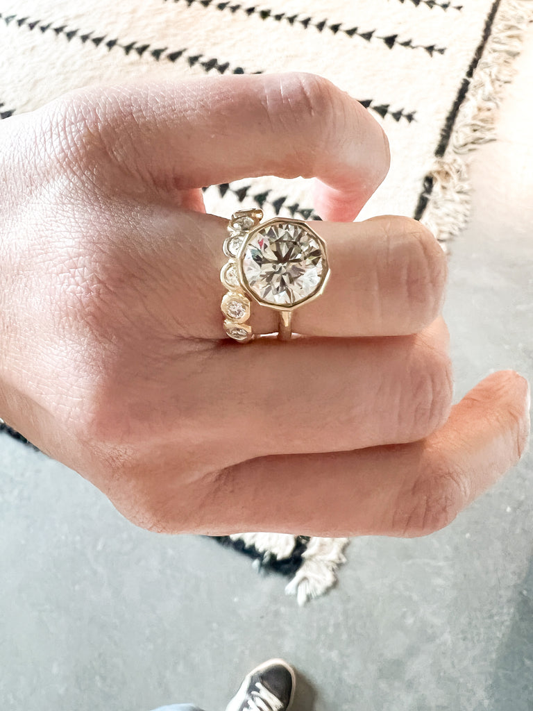 close up of hand wearing gold ring with decagon bezel set round brilliant diamond alongside diamond band