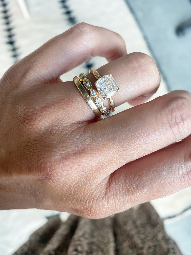 close up of hand wearing gold oval and circle bezel set eternity band with round white diamonds alongside other gold rings