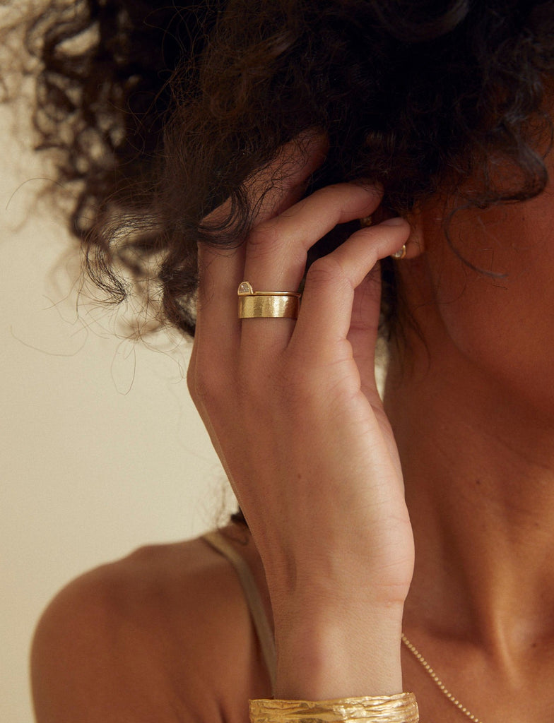 woman wearing lightly textured gold band with straight sides alongside other gold jewelry
