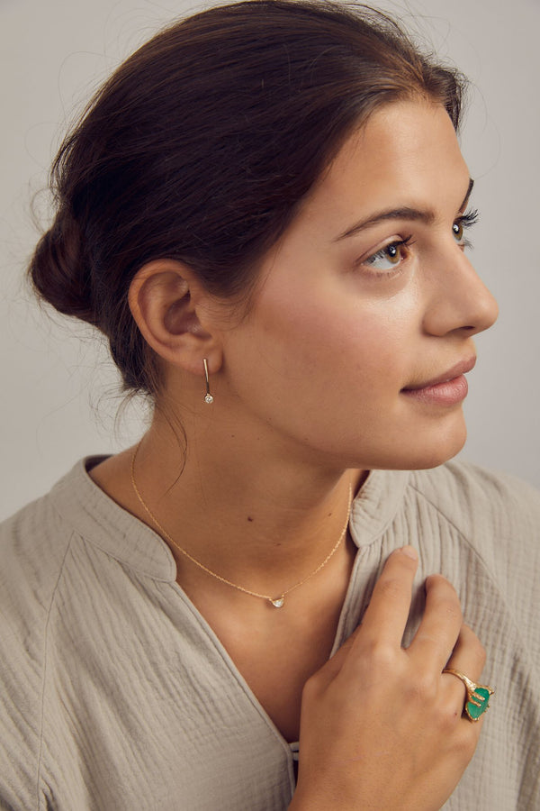 woman wearing gold bar earring with bezel set round white diamond