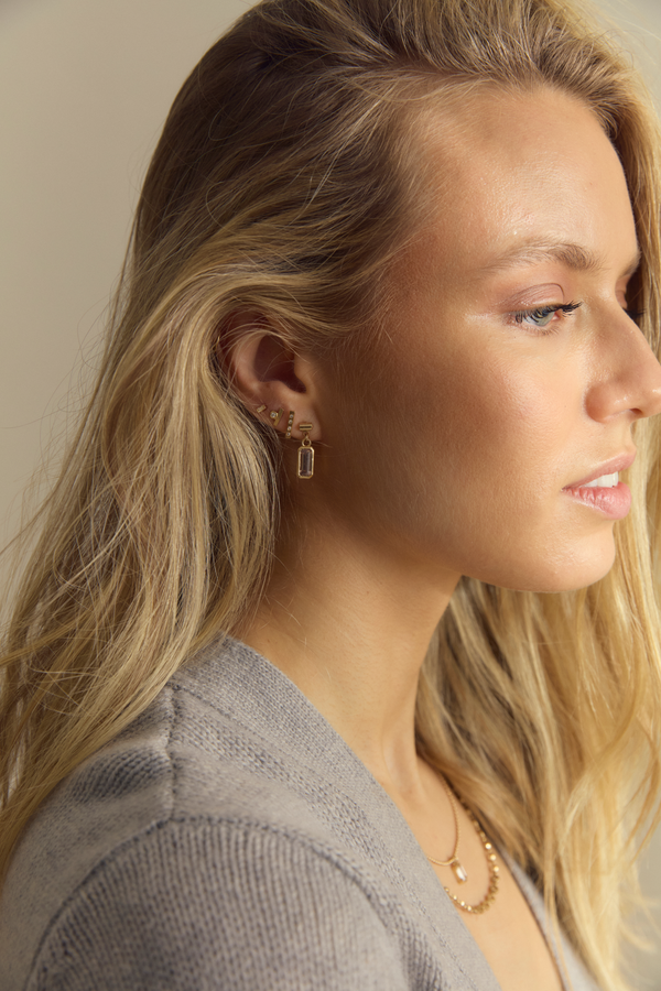 A person wearing a gold bezel set tourmaline drop earring.