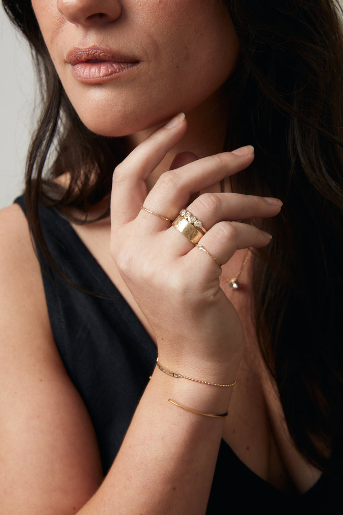 woman wearing thin gold textured band with round diamond alongside other gold jewelry
