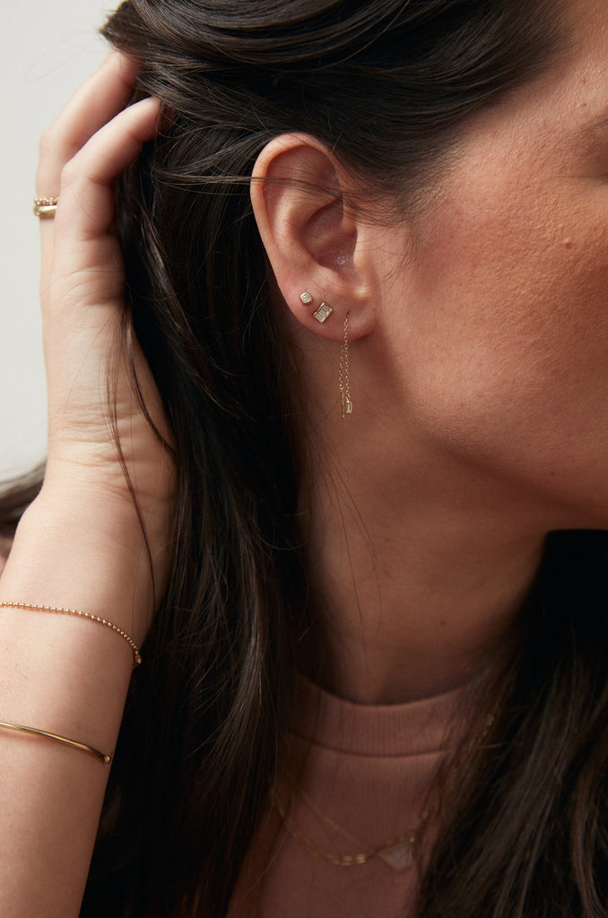 woman wearing gold stud with three baguette white diamonds alongside other gold earrings
