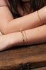 close up of woman wearing flat gold cuff bracelet alongside other gold bracelets
