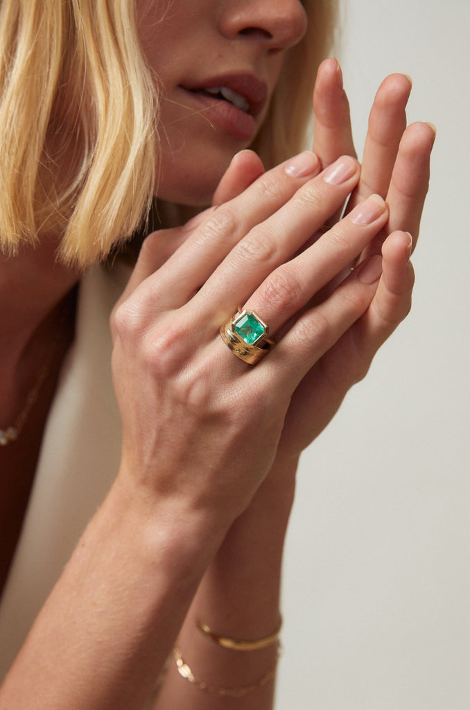 close up of woman wearing Open Bottom Cathedral Bezel set colombian emerald ring with a gold soft knife edge band