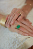 close up of woman wearing gold four prong ring with emerald cut emerald