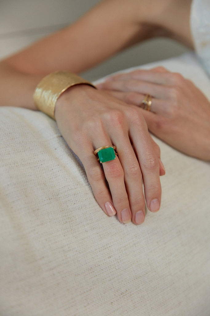 close up of woman wearing gold four prong ring with emerald cut emerald