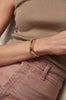 close up of wrist wearing two gold knife edge cut cuffs alongside diamond studded cuff