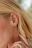 close up of woman wearing gold climber earring with round bezel set white diamond stud