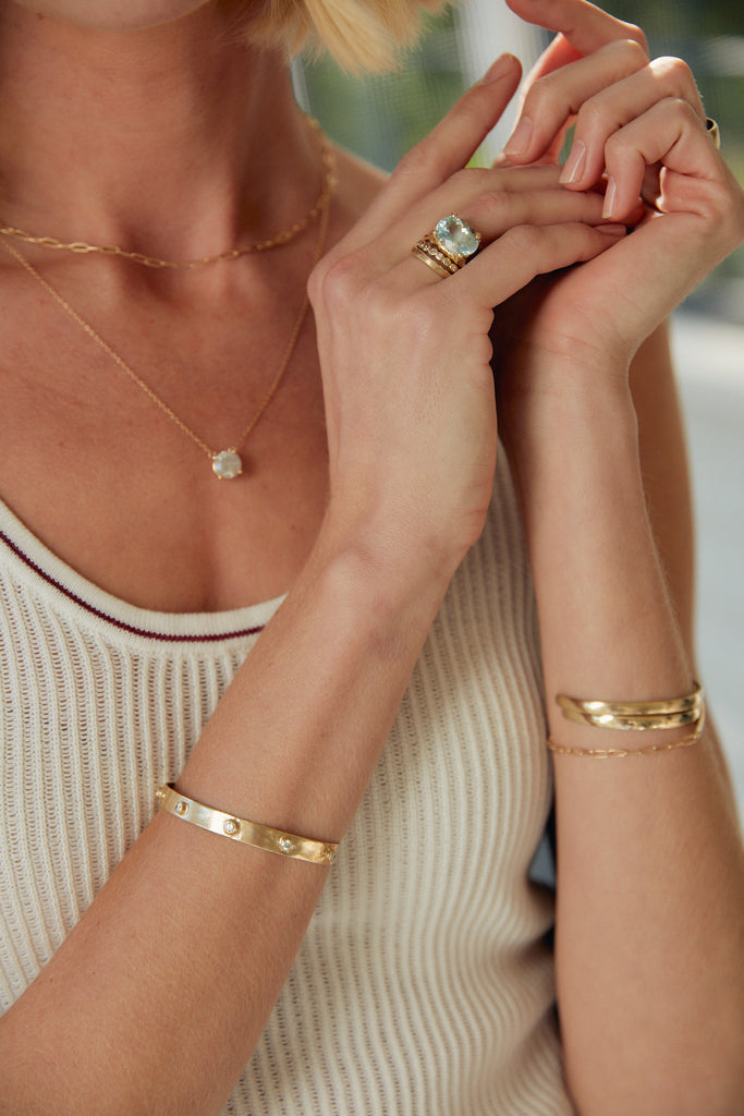 woman wearing gold split textured band with oval aquamarine alongside other gold jewelry
