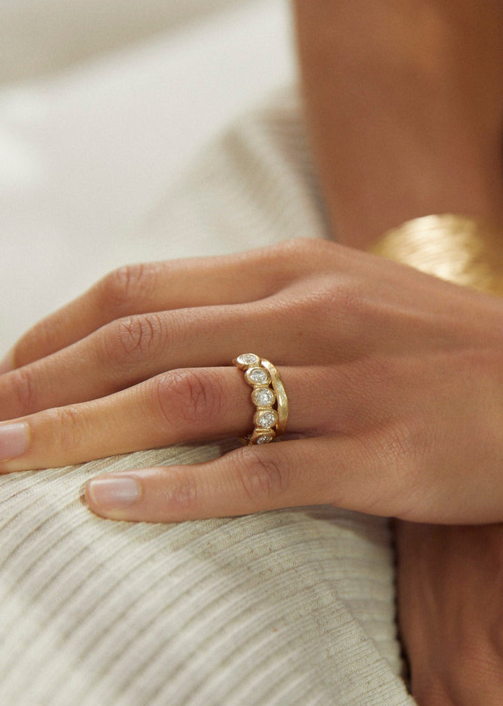 close up of woman wearing rounded gold band alongside other gold ring