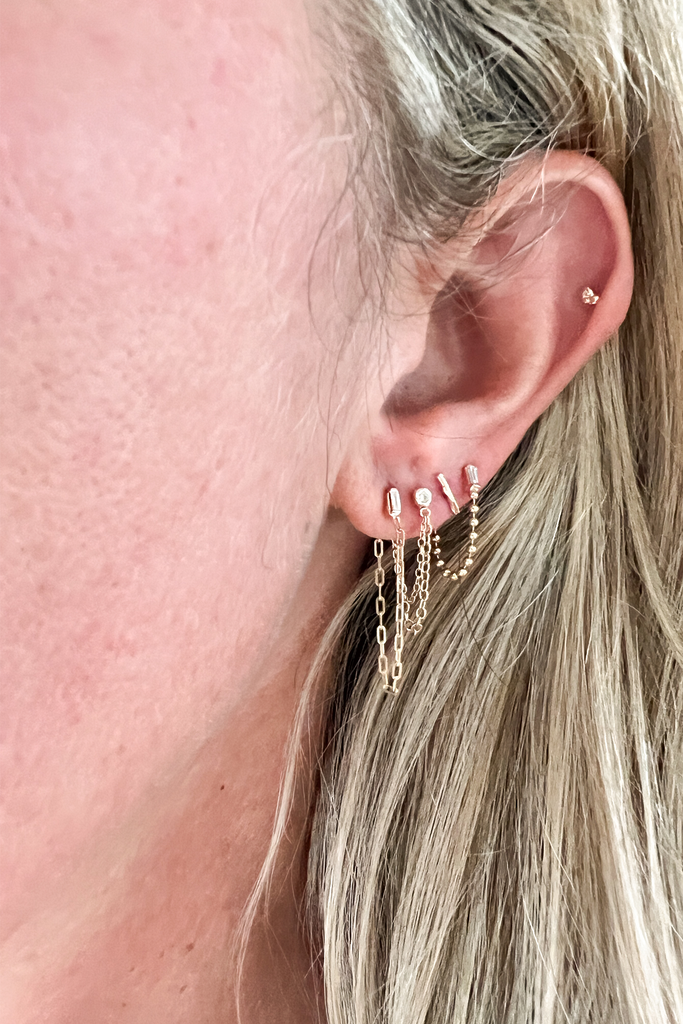 close up of woman's ear with double chain hoop earring with bezel set round diamond among other earrings