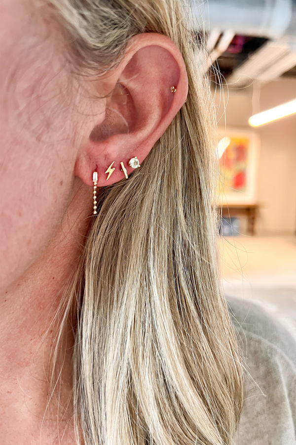 close up of woman wearing ball chain drop stud with white baguette diamond alongside other earrings