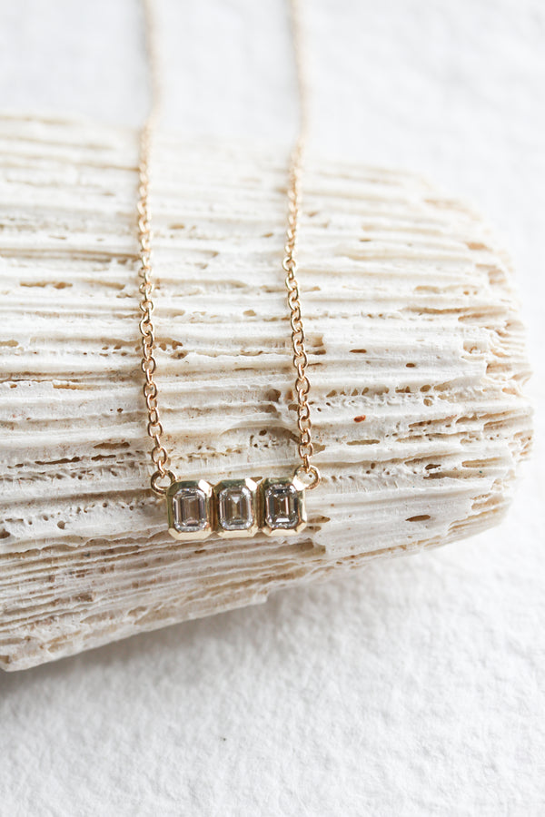 14k yellow gold emerald cut diamond necklace with bezel setting surrounding three diamonds