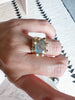close up of hand wearing gold ring with xl prongs and labradorite