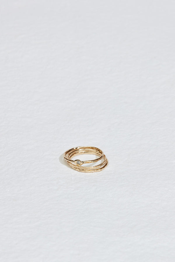stack of thin gold textured bands with a round white diamond on top band
