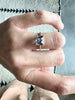 close up of hand wearing emerald cut violet sapphire cathedral set gold ring