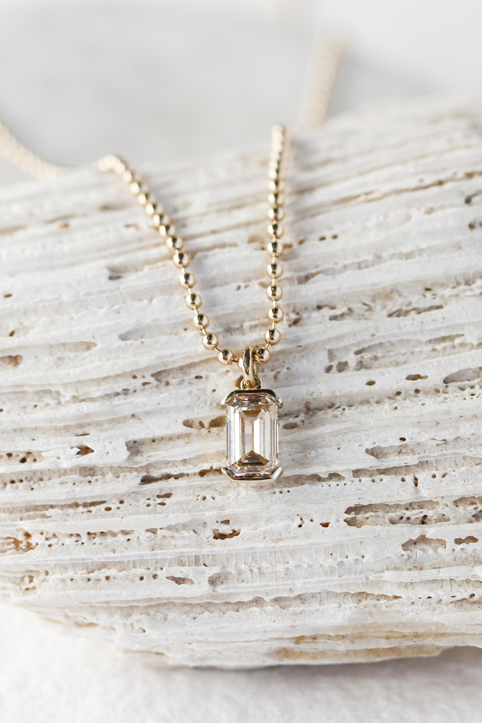 close up of gold ball chain necklace with partial bezel set emerald cut diamond