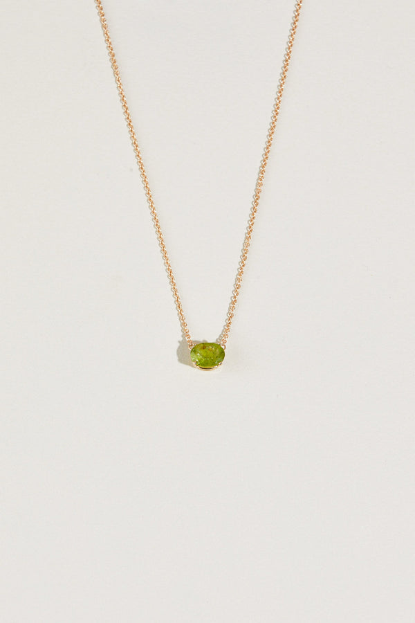 close up of gold necklace with oval peridot