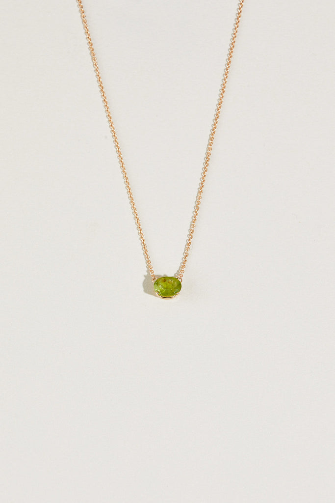 close up of gold necklace with oval peridot