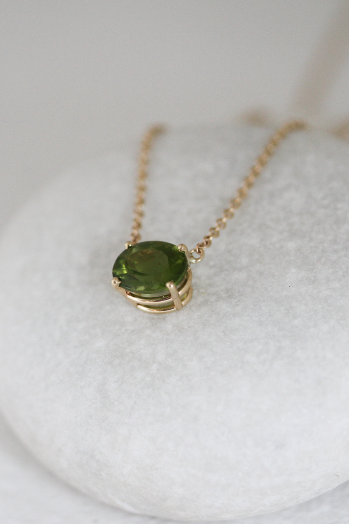 close up of gold necklace with oval peridot