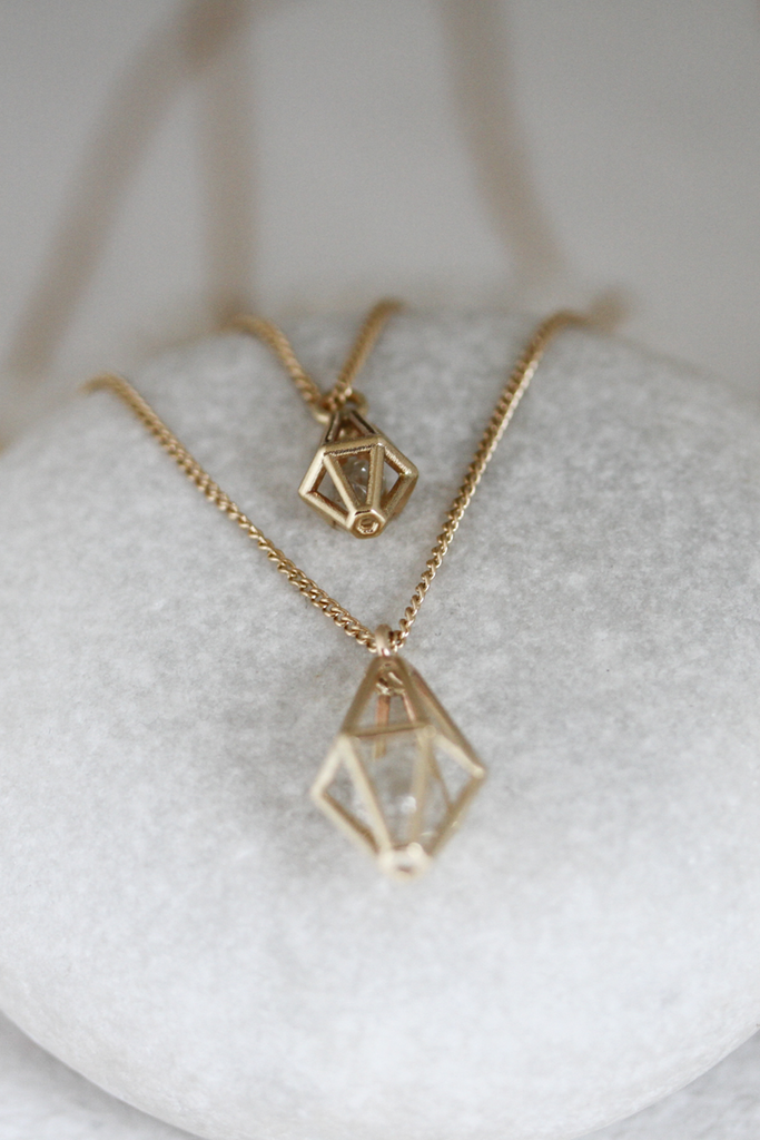 close up of two gold curb chain necklaces with caged raw diamond
