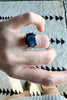 close up of hand wearing 8 prong gold ring with oval deep blue sapphire