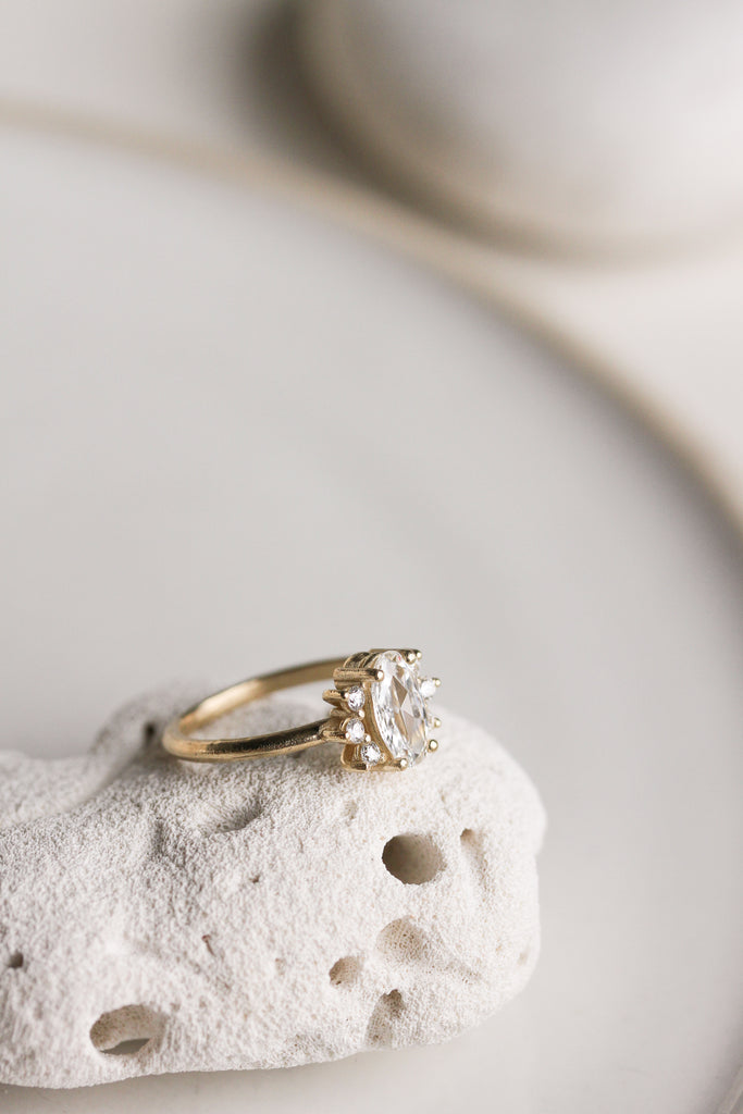 side view of gold ring with elongated rose cut oval diamond and round white diamonds