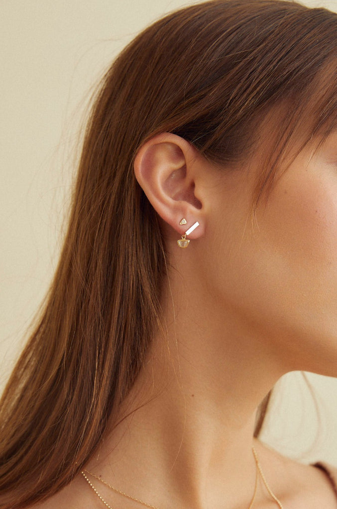 close up of woman wearing gold triangle earring studded with bezel set round white diamond alongside other gold earring