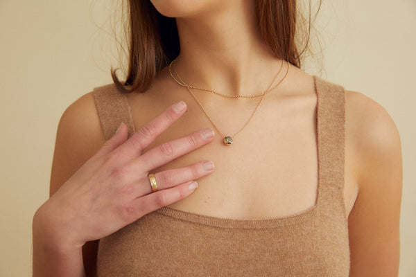 close up of woman wearing gold necklace with round mocha diamond alongside ball chain necklace and gold band