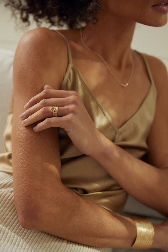 woman's hand wearing gold ring with bezel set oval champagne diamond alongside other gold jewelry