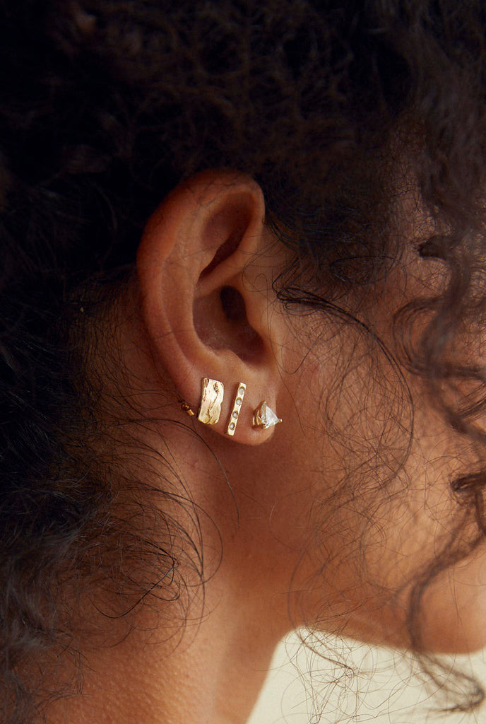 close up of woman wearing gold mini bar stud with round white diamonds alongside other gold earrings