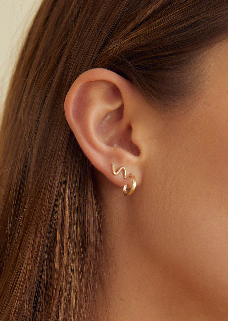 close up of woman wearing gold straight cut hoop earring alongside other gold earring
