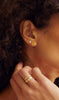 close up of woman wearing round citrine stud with gold three prong martini setting alongside other gold earrings