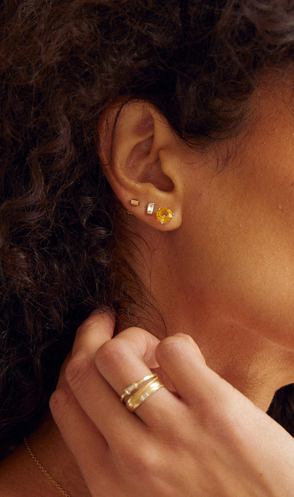 close up of woman wearing gold tube shaped stud alongside other gold jewelry