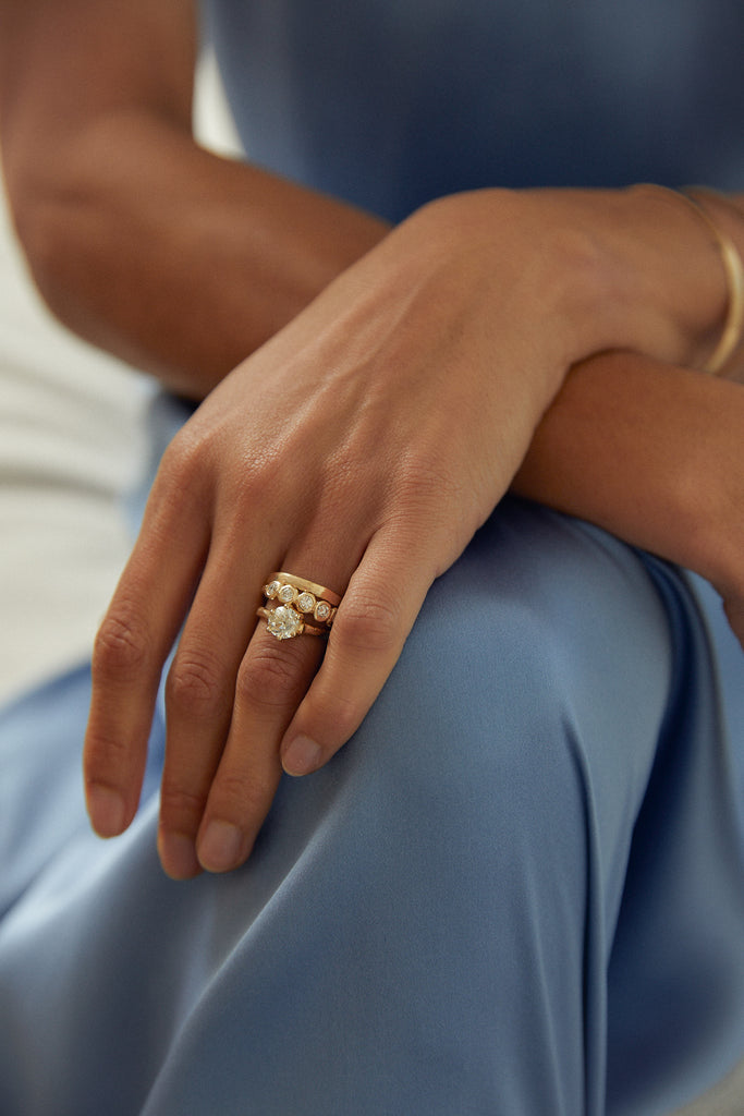 close up of woman wearing gold six prong ring with old euro cut round diamond alongside other gold bands