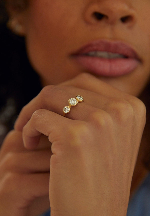 close up of woman wearing gold ring with three bezel set round white diamonds