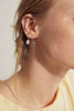 woman wearing gold hoop earring with white opal alongside other gold earrings