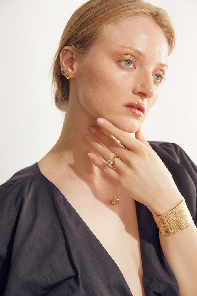 woman wearing round citrine stud with gold three prong martini setting alongside other gold jewelry