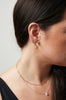 close up of woman wearing gold knife edge cut hoop earrings alongside other gold jewelry