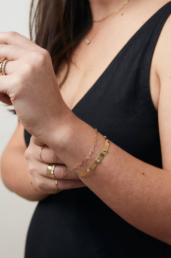 close up of woman wearing gold cable link chain bracelet alongside other gold jewelry