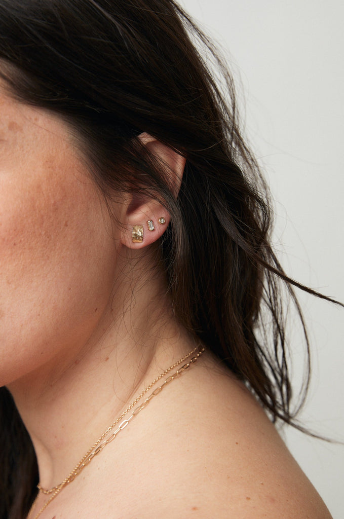 close up of woman wearing gold stud with free form gold plate alongside other gold jewelry