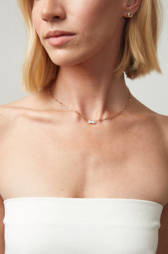 close up of woman wearing gold cable chain necklace with 5 baguette diamonds