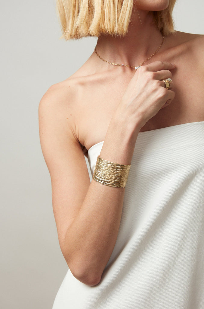 woman wearing thick gold cuff bracelet alongside other gold jewelry
